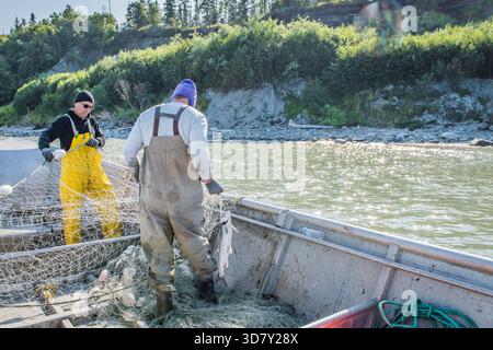 Ein lächelnder kommerzieller Fischer in gelben Lätzchen, der einen frischen Wildlachs auf einem Boot hält, Kalgin Island, Alaska. Stockfoto