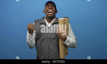 Mann, der gerollte Blaupausen im linken Arm hält und rechte Faust mit geschlossenen Augen geballt, Studio; Determination fokussiert. Stockfoto