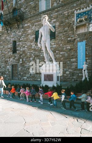 Eine Gruppe von Kindergartenkindern marschiert hintereinander vor der Marmorstatue Davids vor dem Palazzo Vecchio, Florenz, Toskana, Italien Stockfoto