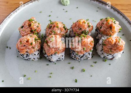 Scharfe Lachs-Maki-Brötchen mit gehacktem Schnittlauch und Sesamsamen auf einer Leuchtplatte Stockfoto