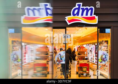 Bamberg, Deutschland 27. November 2025: Im Bild: Blick in den Eingangsbereich einer dm Drogerie in der Bamberger Innenstadt. Vor dem Geschäft kommt ein Fahrzeug oder Objekt vorbei und erzeugt Bewegungsunschärfen im Vordergrund, während sich die Kunden im Inneren befinden Stockfoto