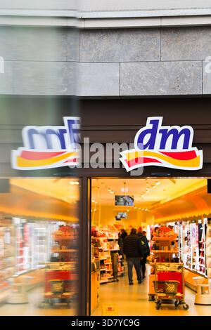 Bamberg, Deutschland 27. November 2025: Im Bild: Blick in den Eingangsbereich einer dm Drogerie in der Bamberger Innenstadt. Vor dem Geschäft kommt ein Fahrzeug oder Objekt vorbei und erzeugt Bewegungsunschärfen im Vordergrund, während sich die Kunden im Inneren befinden Stockfoto