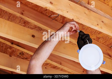 Der Elektriker befestigt die Beleuchtungskörper an der Decke in der Renovierungsanlage zu Hause, um Details zur Sicherheit zu erhalten. Stockfoto