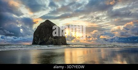 Atemberaubender Sonnenuntergang am Haystack Rock am Cannon Beach mit buntem Himmel und Reflexionen vom ruhigen Wasser am Strand Stockfoto