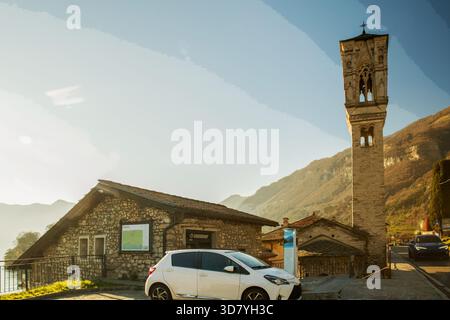 Asphaltstraße entlang der Küste von Como nach Norden und hoher Glockenturm der katholischen Kirche. Leute, die UNS wehkelten, wandern auch mit chinesischer Ethnizität Stockfoto