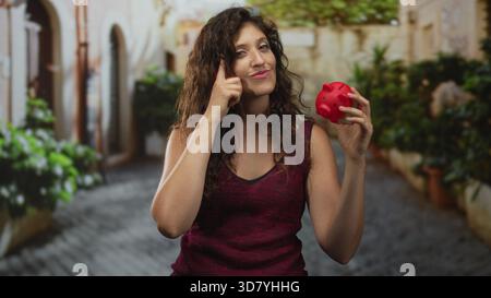 Die Frau zeigt mit dem Finger auf den Tempel, während sie auf der Kopfsteinpflasterstraße die rote Schweinebank hält. Stockfoto