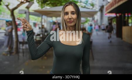 Frau zeigt auf der Terrasse des Restaurants mit dem Finger auf die Straße, sichtbare Hand und Zeigefinger zeigen in Geste; ruhige Selbstentscheidung. Stockfoto