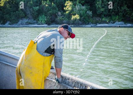 Kommerzielle Fischer in gelben Lätzchen, die ein langes Kiemennetz in den Küstengewässern von Cook Inlet, Kalgin Island, Alaska, beobachten. Stockfoto