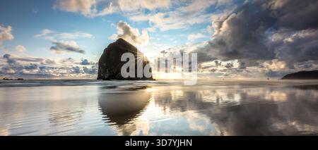 Atemberaubender Sonnenuntergang am Haystack Rock am Cannon Beach mit buntem Himmel und Reflexionen vom ruhigen Wasser am Strand Stockfoto