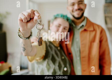 Ein junges multiethnisches Paar lächelt, während er nach dem Einzug in die Heimat die Schlüssel hält Stockfoto