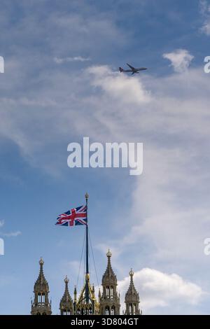 London, England, Großbritannien - 4. Juli 2025: Spitze des Turms auf den Houses of Parliament mit der Flagge der Union Jack und einem Flugzeug über dem Haus Stockfoto