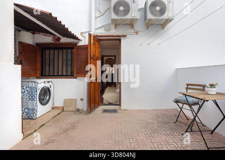 Innenhof im Freien mit Waschmaschine, Fliesenboden, Klapptisch und Zugang zu Holztüren. Stockfoto