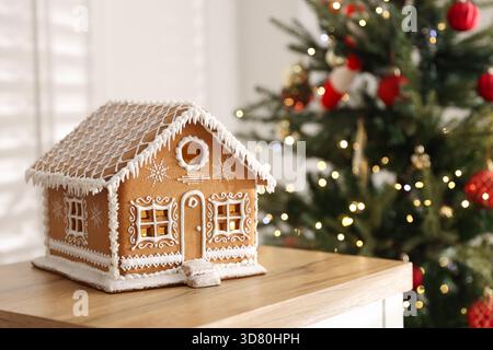 Wunderschönes Lebkuchenhaus auf Holzkommode vor verschwommenem Licht drinnen, Nahaufnahme. Leerzeichen für Text Stockfoto