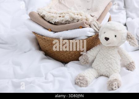 Wäschekorb mit gefalteter Kleidung und Spielzeug auf Bettwäsche, Nahaufnahme Stockfoto