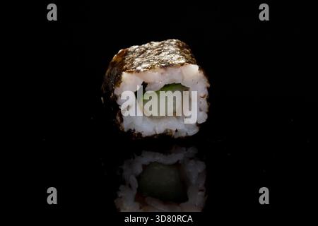 Eine Rolle mit Gurke steht auf einer glänzend schwarzen Oberfläche Stockfoto