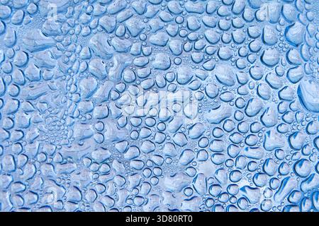 Abstrakter Hintergrund mit einer Makroansicht von Wassertropfen auf einer blauen Oberfläche, die ein natürliches Muster von Feuchtigkeit und Kondensation erzeugt. Stockfoto
