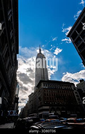 Das Empire State Building erhebt sich vor einem klaren blauen Himmel und schafft eine atemberaubende Silhouette in Manhattan. Wolken verleihen der Skyline-Ansicht Tiefe. Stockfoto