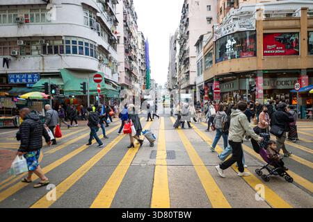Geschäftige Straßenkreuzung in Hongkong. Fußgänger überqueren die Straße an einer überlasteten Kreuzung und zeigen die temporeiche Natur des städtischen Lebens in der Stadt. Stockfoto