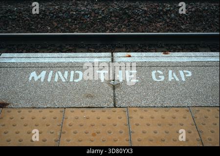 Nahaufnahme des Geistes der Gap-Warntext auf einem Bahnsteig in der Nähe von Bahngleisen. Erinnerung an die Reisesicherheit im britischen Transportsystem. Stockfoto