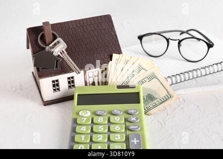 Hausmodell, Schlüssel, Geld und Taschenrechner auf weißem Tisch Stockfoto