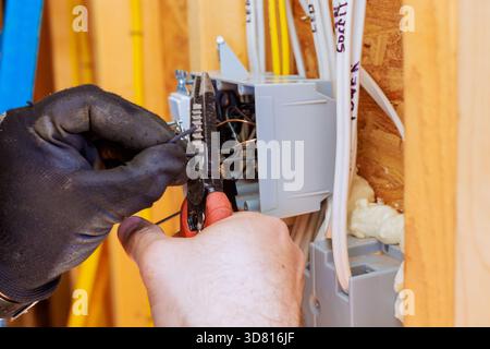 Elektriker mit Bohrwerkzeugen zum Anschließen von Drähten am Leistungsschalter während der Hausbauarbeiten. Stockfoto