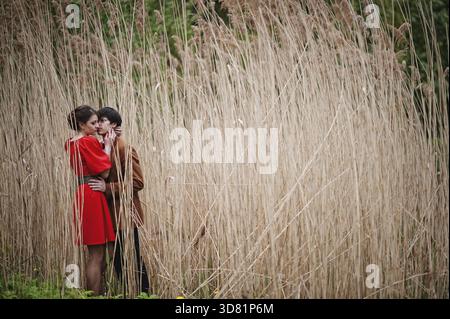 Paar umarmt an Liebe auf den hohen Stock. Stilvolle Mann am Samtjacke und Mädchen im roten Kleid in Liebe zusammen Stockfoto