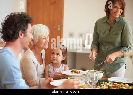 Lächeln, Servieren und Liebe mit der Familie beim Mittagessen für Bonding, Ernährung und Thanksgiving. Großmutter, Mädchen und geselliges Treffen mit Vater zu Hause Stockfoto