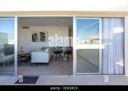 Modernes, offen geschnittenes Wohn- und Esszimmer mit Blick von der Terrasse durch große Glastüren. Stockfoto