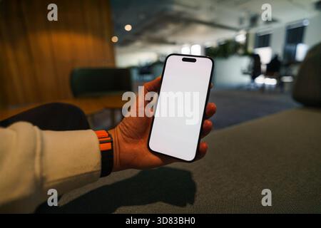 Smartphone Mockup Lounge Büro Hand leerer Bildschirm. Entspanntes, professionelles Ambiente mit modernen Sitzen und verschwommenem Hintergrund, perfekt für Präsentationen Stockfoto