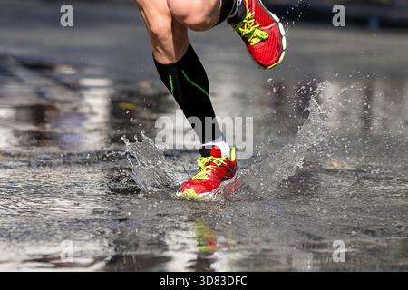Lauffüße in Kompressionsstrümpfen, die in Wasserspritzern auf Asphalt laufen Stockfoto