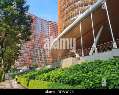 Geschwungenes modernes Hochhaus mit grünem urbanem Fußweg und Bäumen, das zeitgenössische Architektur und eine saubere Stadtumgebung zeigt. Stockfoto