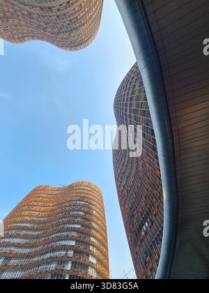 Dramatischer Blick nach oben auf moderne geschwungene Türme vor blauem Himmel, der zeitgenössische Architektur, Geometrie und vertikales Stadtdesign hervorhebt. Stockfoto