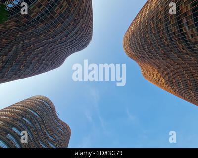Blick nach oben auf vier organische geschwungene Hochhäuser, die einen geometrischen Rahmen vor dem blauen Himmel bilden und moderne Architektur und urbanes Design zeigen. Stockfoto