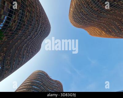 Moderne geschwungene Hochhäuser, die den Himmel nach oben umrahmen und zeitgenössische architektonische Formen und Stadtdesign hervorheben. Stockfoto