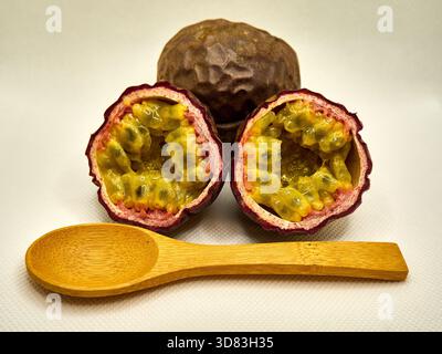 Komplette Passionsfrucht-Zusammensetzung: Ganze Früchte, geschnittene Hälften und Holzlöffel Stockfoto