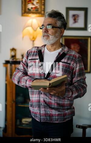 Ein Mann hält ein Buch in einem gemütlichen Wohnzimmer voller Kunst Stockfoto