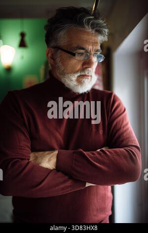 Mann mit silbernen Haaren und Bart, der einen kastanienbraunen Rollkragenpullover trägt Stockfoto