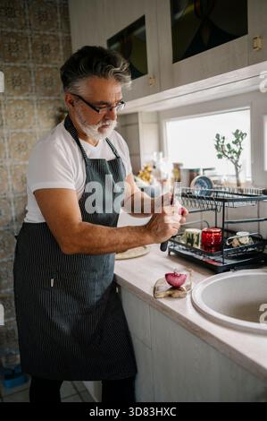 Ein Mann mittleren Alters bereitet Zutaten in einer gemütlichen Küche zu Stockfoto