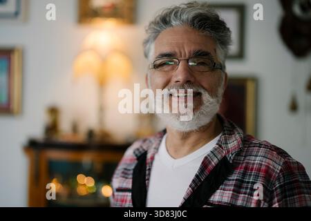 Ein älterer Mann lächelt in einem gemütlichen, schön eingerichteten Wohnzimmer Stockfoto
