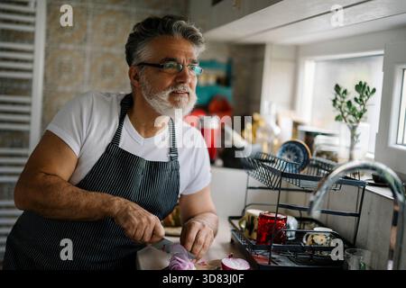 Ein Mann, der eine Mahlzeit in einer hellen Küche zubereitet, während er Gemüse hackt Stockfoto