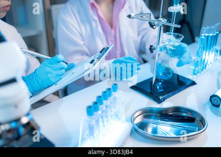 Zwei Chemiker in weißen Labormänteln arbeiten in einem modernen Labor zusammen, umgeben von wissenschaftlichen Geräten, Computern und Glaswaren, die Tee repräsentieren Stockfoto