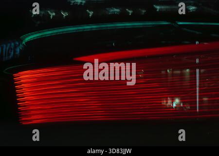 Eine lange Belichtungsaufnahme roter Rücklichter, die ein Gefühl von Geschwindigkeit und Bewegung auf einer dunklen Straße erzeugt. Stockfoto