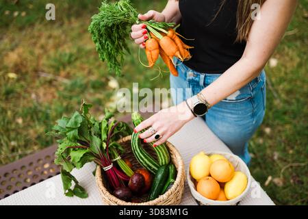 Frau, die Karotten neben Körben mit frischen Gartenprodukten hält Stockfoto