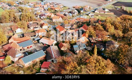 Ländliche Dorfgebäude umgeben von bunten Herbstbäumen mit vielen Solarpaneelen auf Dächern, die erneuerbare Energien betonen Stockfoto