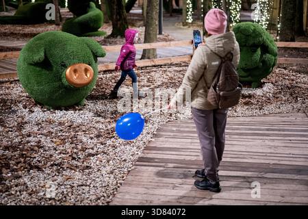 Eine Frau fotografiert ein Mädchen, das aus einer schweinähnlichen Sphäre im National Expocenter of Ukraine Complex (VDNG), Kiew, Ukraine, am 27. November 2025 geht. Am 29. November wird die elfte Staffel des Winter Country Projekts bei der VDNG eröffnet. Auf dem zentralen Platz des Nationalen Expozentrums der Ukraine können Besucher eine Winterrutsche, ein Riesenrad, ein Karussell und andere Attraktionen genießen. In der Nähe wird eine Weihnachtsmesse zum Leben erweckt, während ein Food Court nur einen kurzen Spaziergang entfernt festliche Köstlichkeiten bietet. (Foto: Danylo Antoniuk/Ukrinform) Stockfoto