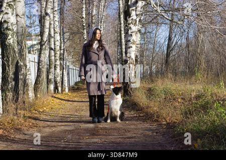 Eine junge Indianerin steht auf einem Waldweg mit ihrem Hund an ihrer Seite und genießt einen friedlichen Tag in der Natur Stockfoto