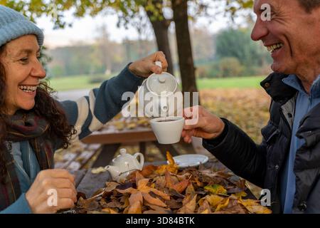 Glückliches Seniorenpaar, das bei einem Herbstpicknick im Park Tee teilt Stockfoto