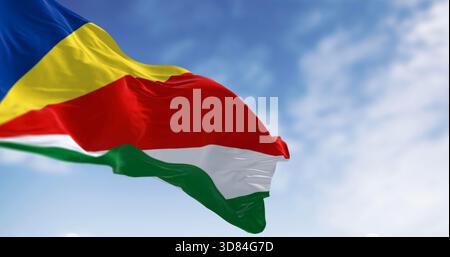 Die Nationalflagge der Seychellen winkt an einem klaren Tag im Wind. Fünf schräge Bänder in Blau, Gelb, Rot, weiß und Grün. 3D-Darstellung. Gewelltes Material Stockfoto