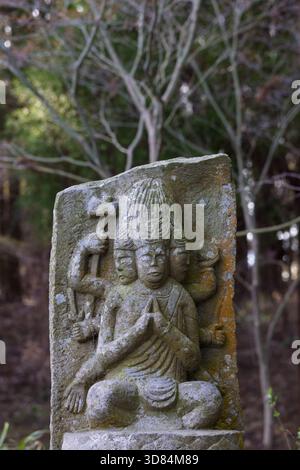 Kleine verwitterte Buddha-Skulpturentafel mit Murti-Figur mit mehreren Gesichtern und Armen, die verschiedene Kräfte im Saigandenji-Tempel in Little VI symbolisieren Stockfoto