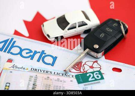 Alberta canadian Autokennzeichen und Zündschlüssel auf der Flagge von Kanada Nahaufnahme. Führerschein- und Zulassungskonzept Stockfoto